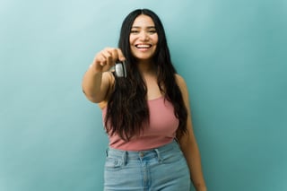 Hispanic young woman extending a car key toward the camera, smiling and celebrating her new car purchase